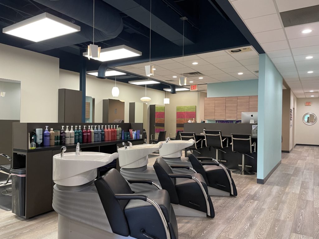- Bella Salon in Madison, WI Modern salon interior featuring three black shampoo chairs, sinks, shelves stocked with hair products, and a reception desk in the background—perfect for expert hair cuts and vibrant hair color services. - Bella Salon in Madison, WI