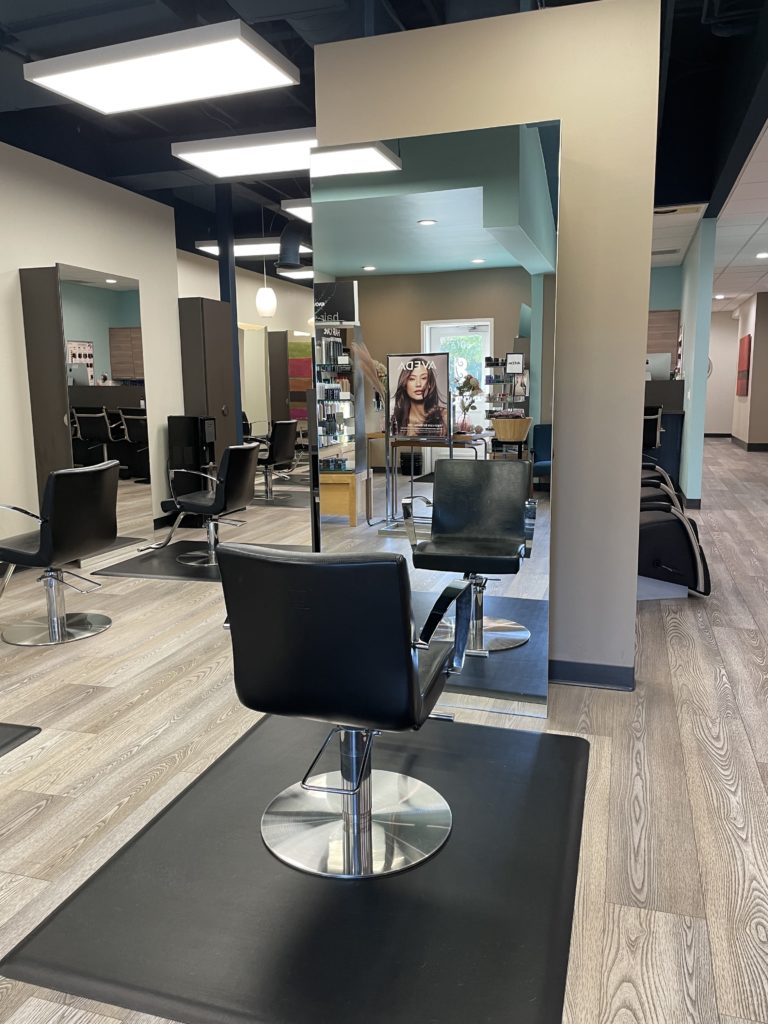 - Bella Salon in Madison, WI Interior of a modern hair salon with empty black styling chairs, large mirrors, and wooden flooring. Hair products focused on plant based hair care and a model poster are visible in the background. - Bella Salon in Madison, WI